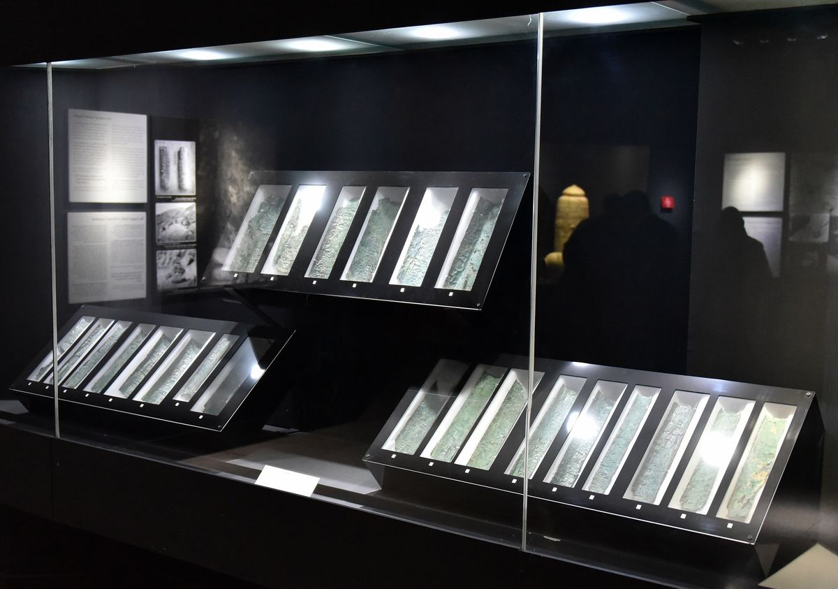 Museum cases holding curved, corroded copper strips under soft light